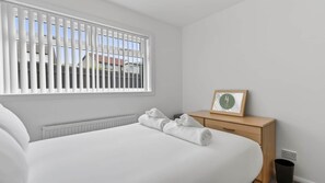 Ein Hotelzimmer mit einem Bett, einem Nachttisch mit einem gerahmten Bild und einem Fenster mit Jalousien.