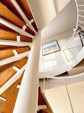 Eine Wendeltreppe mit Holzboden und weißen Geländern, die zu einer Plattform mit einem gerahmten Bild führt.