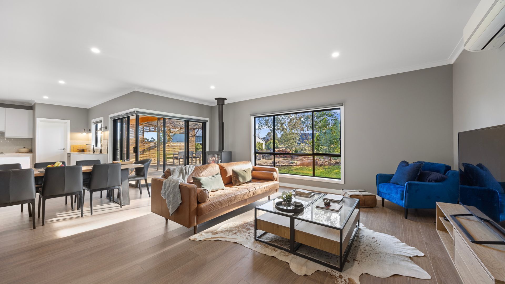 A modern living room with a large window, a dining area, and a kitchen.