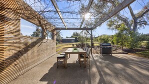 En udendørs terrasse med et træbord og stole, grill og pergola.