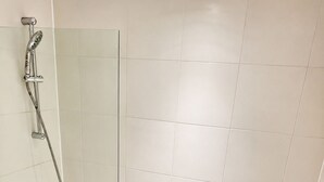 Een moderne badkamer met een douche met glazen wand, een wit bad en een handdouche.