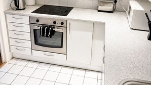 Een keuken met witte kastjes, een roestvrijstalen afzuigkap, een inbouwoven, een broodrooster en een waterkoker.