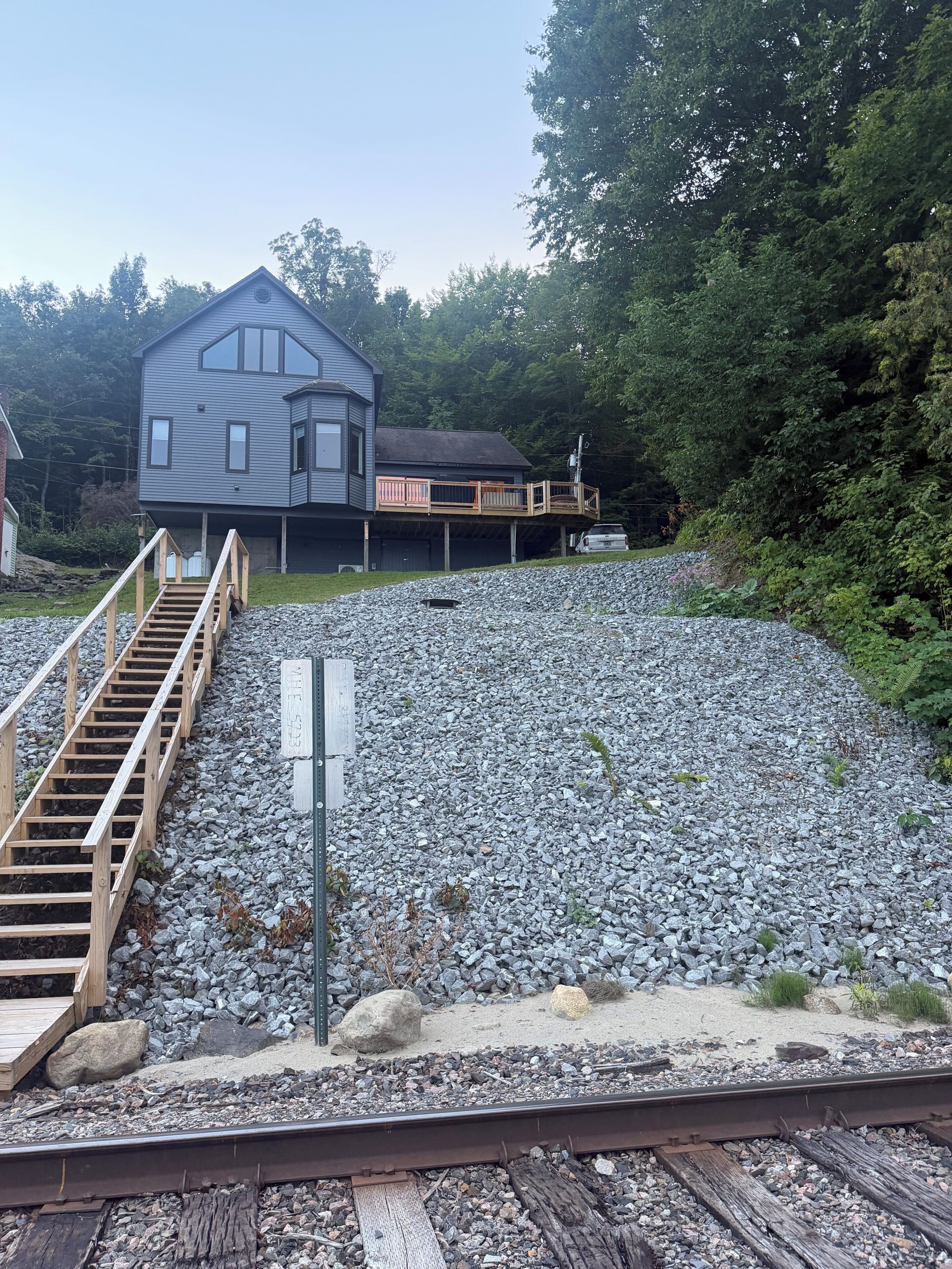 Ein zweistöckiges Haus mit einer Terrasse, einer Schotterauffahrt und einem Bahnweg im Vordergrund.