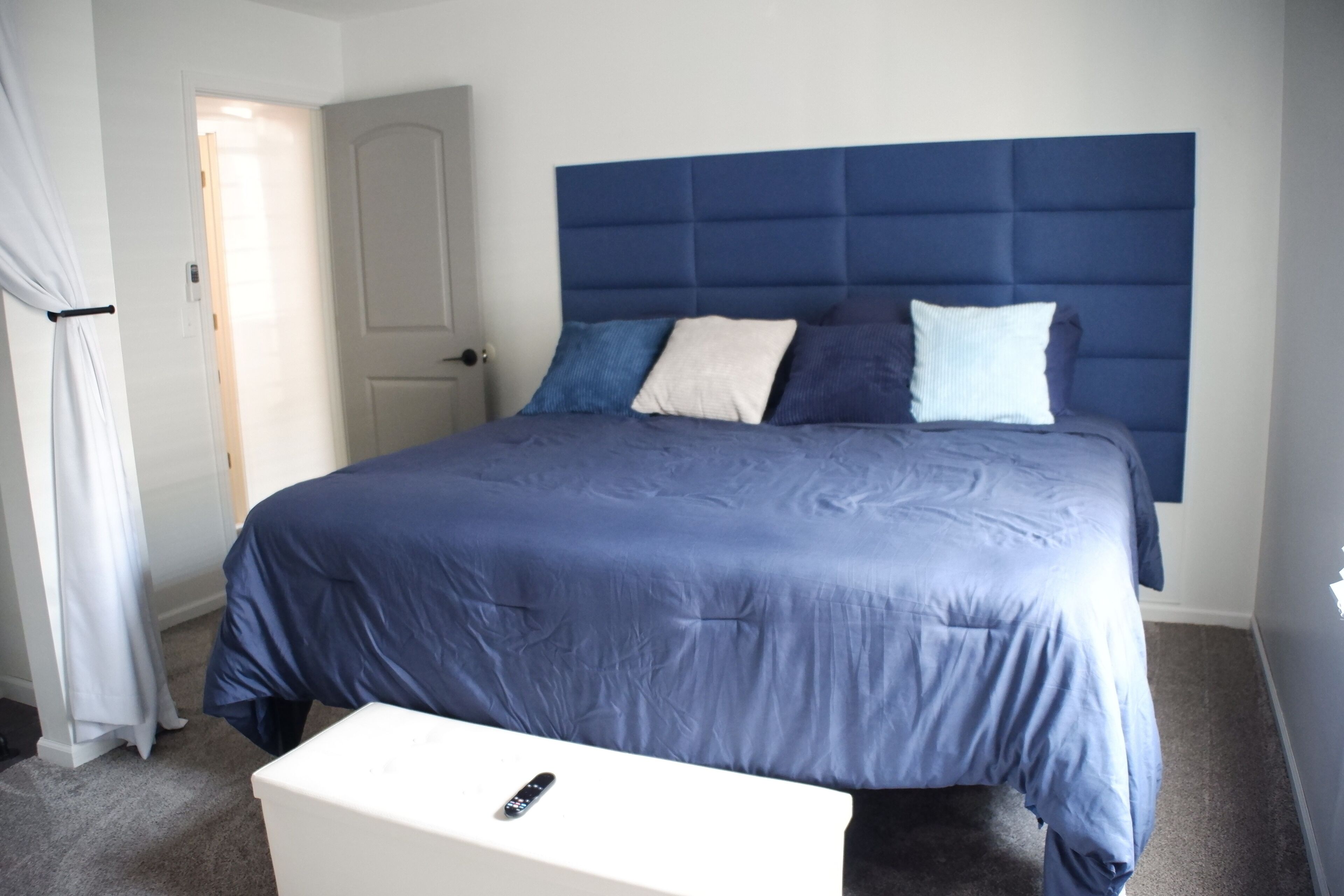 Un dormitorio con una cama grande, una mesita de noche blanca y una puerta al fondo.