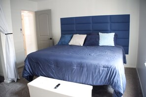 Un dormitorio con una cama grande, una mesita de noche blanca y una puerta al fondo.