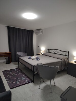 Ein kleines, helles Schlafzimmer mit einem Einzelbett, einem Sessel, einem Schreibtisch und einem Nachttisch.