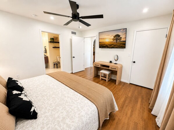 Ein Schlafzimmer mit einem Bett, einem Schreibtisch, einem Stuhl, einem Deckenventilator und einem Bild an der Wand.