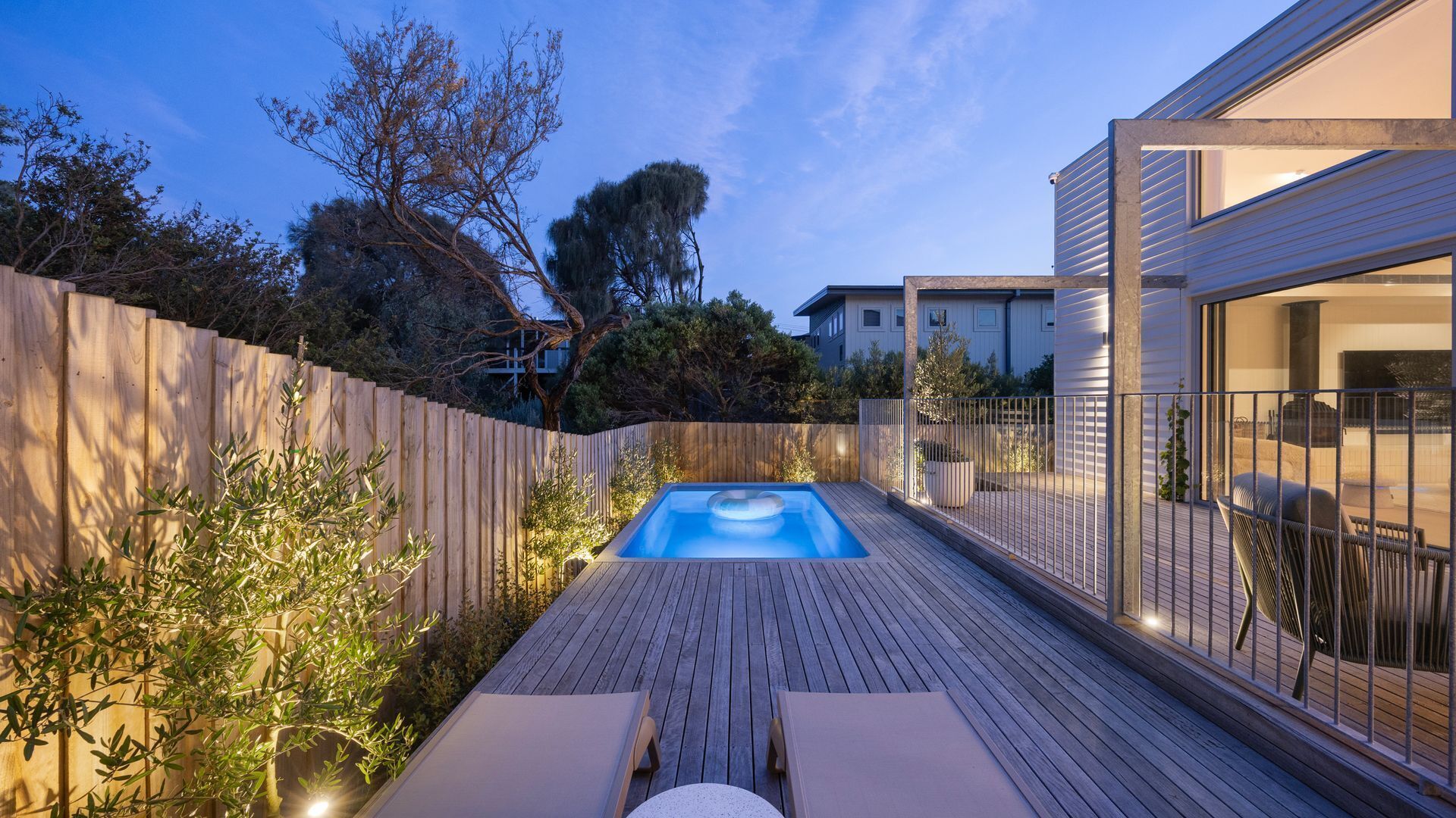 A wooden deck with a hot tub, lounge chairs, and a wooden fence.