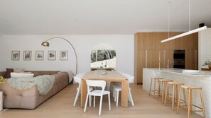 Ein modernes Wohnzimmer mit einer Couch, einem Esstisch mit Stühlen und einer Küchenzeile mit Barhockern.