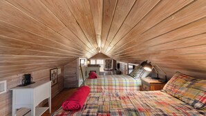 Un dormitorio acogedor en el ático, con listones de madera en el techo, una cama con colcha colorida, una mesita de noche con lámpara y un escritorio pequeño con silla.