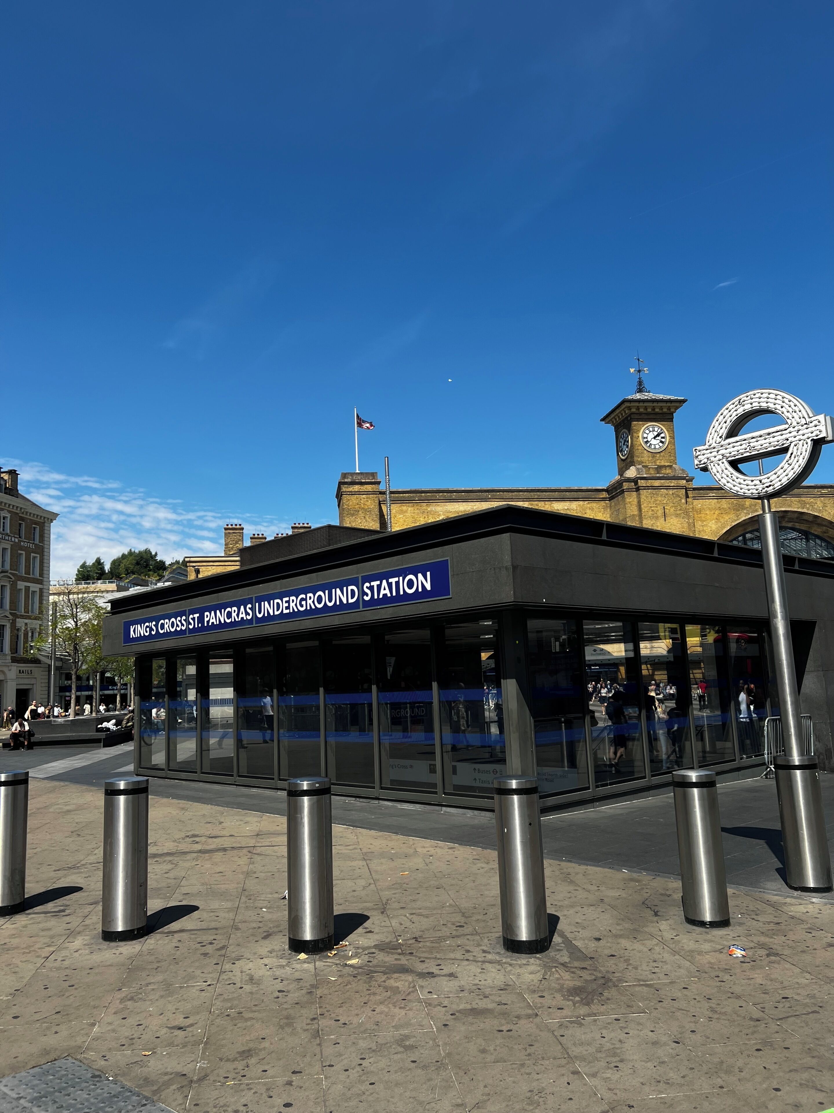 An underground station with a clear sky, a clock tower, and a distinctive round sign.