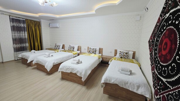 A hotel room with four single beds, a ceiling fan, and a patterned tapestry. - Samarkand City Center Hotel (Samarkand)