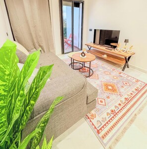 A living room with a sofa, a coffee table, a TV stand, and a patterned rug. - Cozy studio in Palmier with AC and self check in (Casablanca)