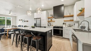 Une cuisine moderne dotée d’un îlot central, de tabourets de bar, d’appareils électroménagers en acier inoxydable et offrant une vue sur l’extérieur.