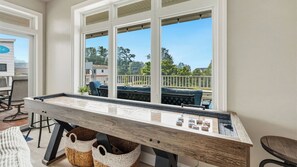 A pool table in a room with large windows, a view of a balcony with outdoor furniture, and a white wall.