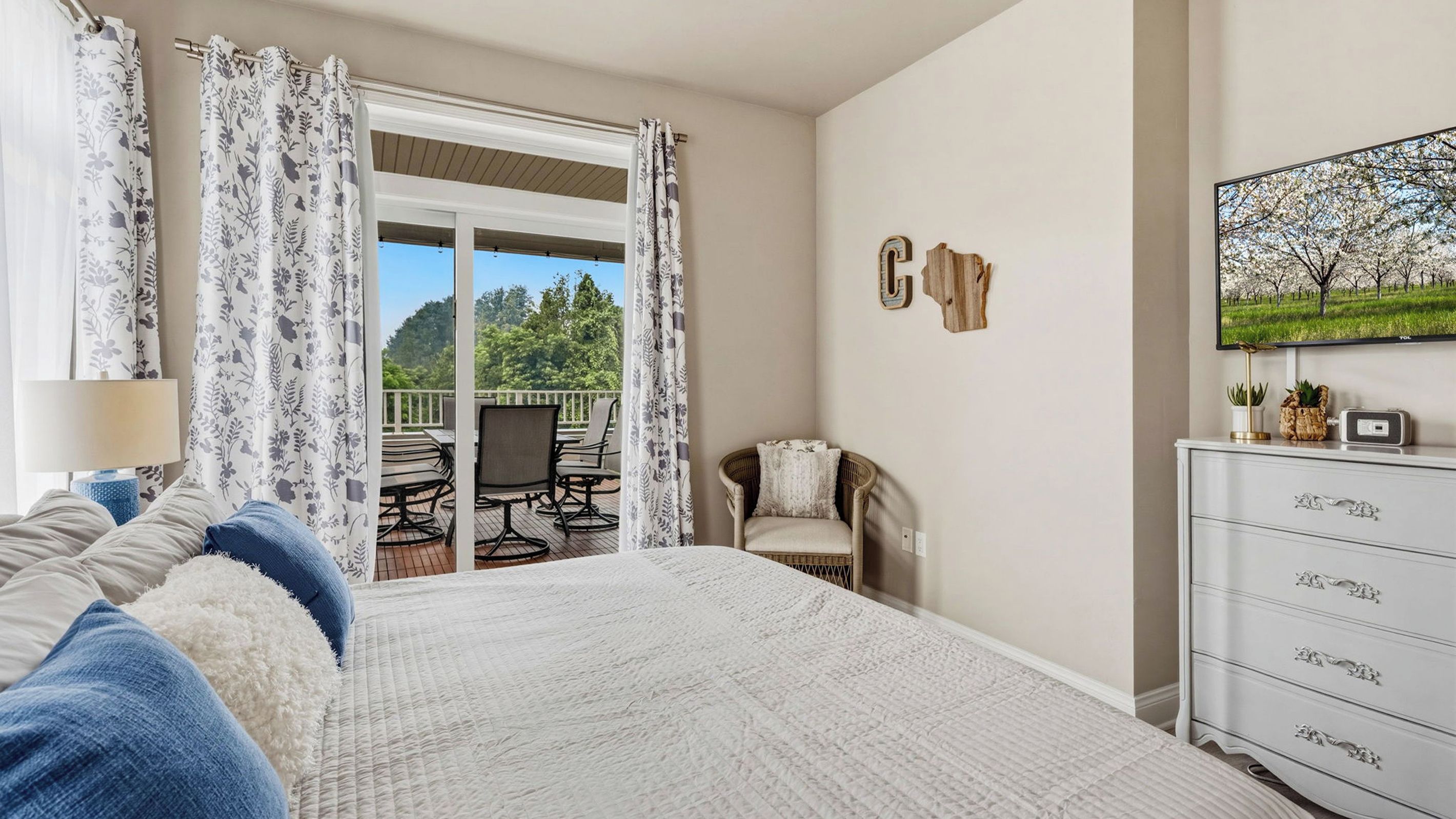 A bedroom with a bed, a chair, a dresser, and a balcony with outdoor furniture.