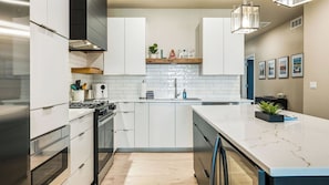 Une cuisine moderne avec des meubles blancs, un plan de travail en marbre et un four encastré.