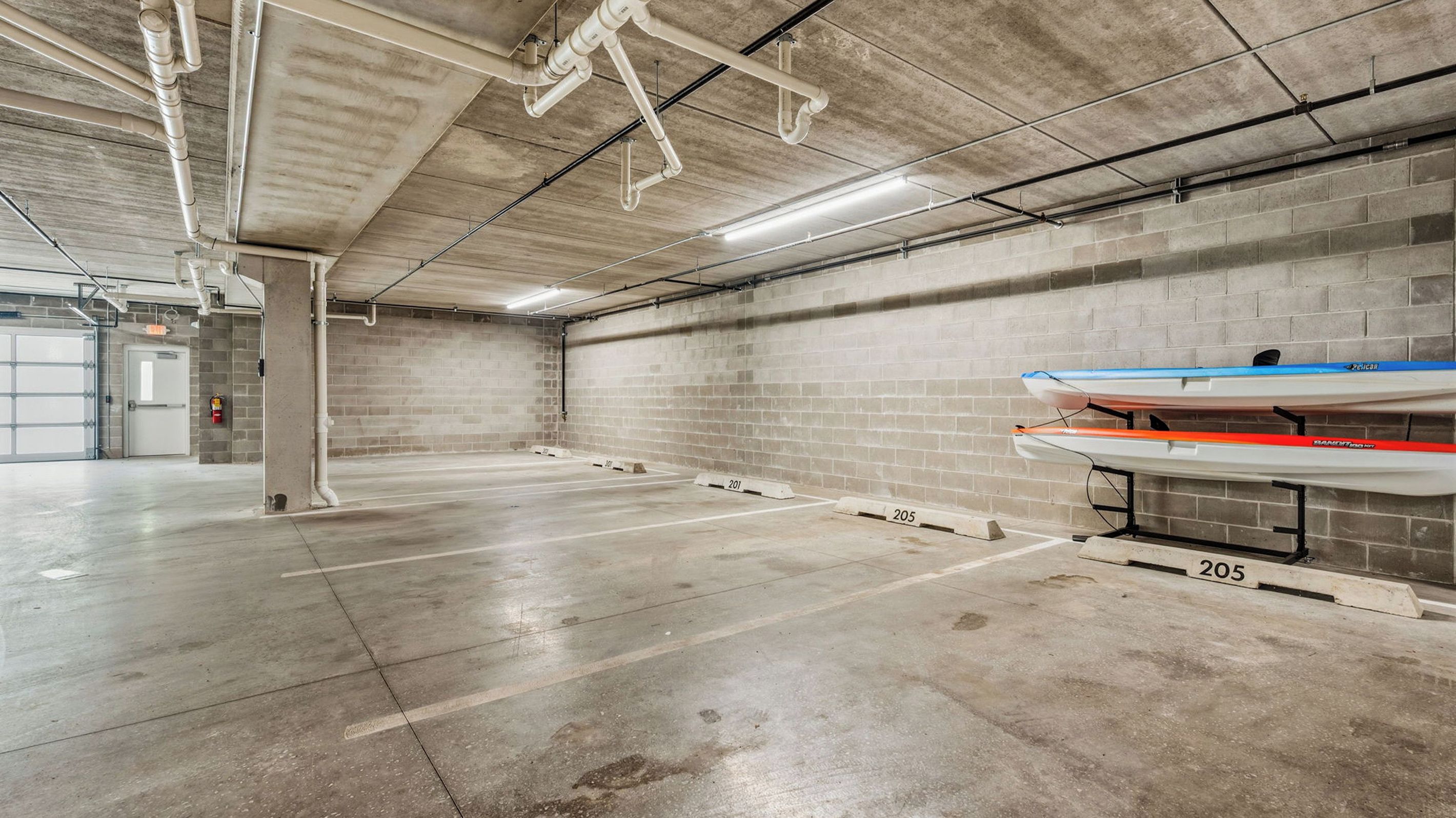 An indoor parking garage with concrete floors and walls, a fire extinguisher, and numbered parking spaces.