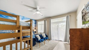 A room with bunk beds, a ceiling fan, a sofa with cushions, a rug, and a large window with curtains.