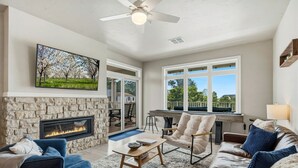 A spacious living room with a stone fireplace, comfortable seating, and large windows offering a view of the outdoors.