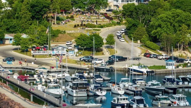A marina with boats docked, a parking area, and a building in the background.