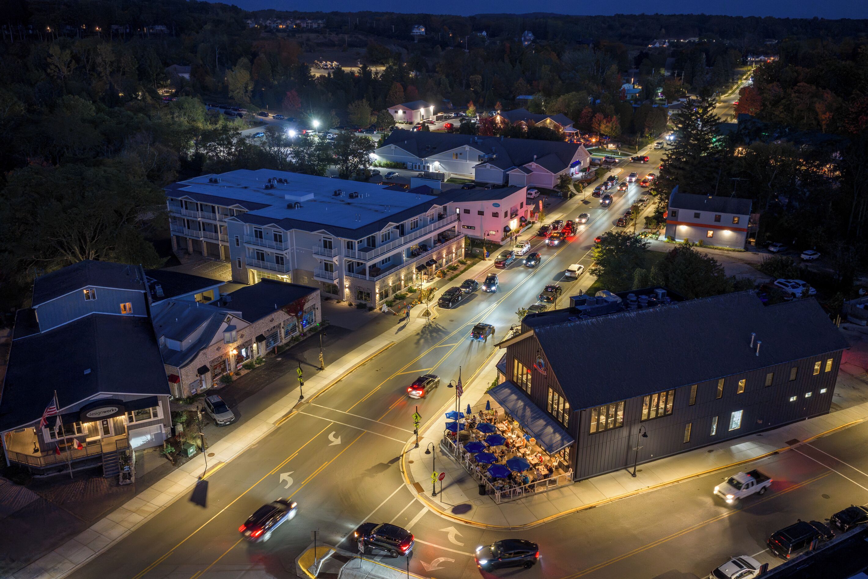 A multi-story building with a flat roof, a parking lot, and a street with cars.