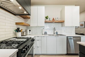 Una cocina moderna con gabinetes blancos, estufa de acero inoxidable y lavavajillas integrado.