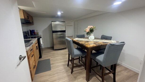 Une cuisine compacte dotée d’un réfrigérateur encastré, de meubles de rangement en bois et d’un coin repas avec une table en marbre et des chaises bleues.