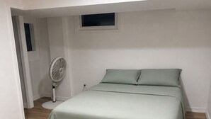 Une chambre à coucher avec un lit, un ventilateur sur pied et une fenêtre.