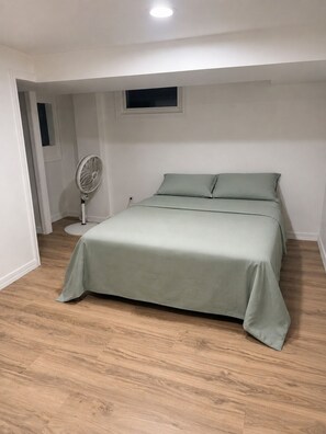 Ein Schlafzimmer mit einem Bett, einem Standventilator und einem Fenster.