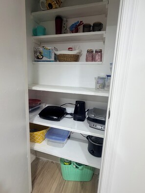 Eine Küche mit weißen Regalen, auf denen diverses Küchengeschirr, ein Toaster und ein Wasserkocher stehen.
