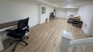 Une pièce spacieuse avec un plancher en bois, un bureau avec une chaise, un lit avec une couverture et une petite table sur laquelle est posé un vase.