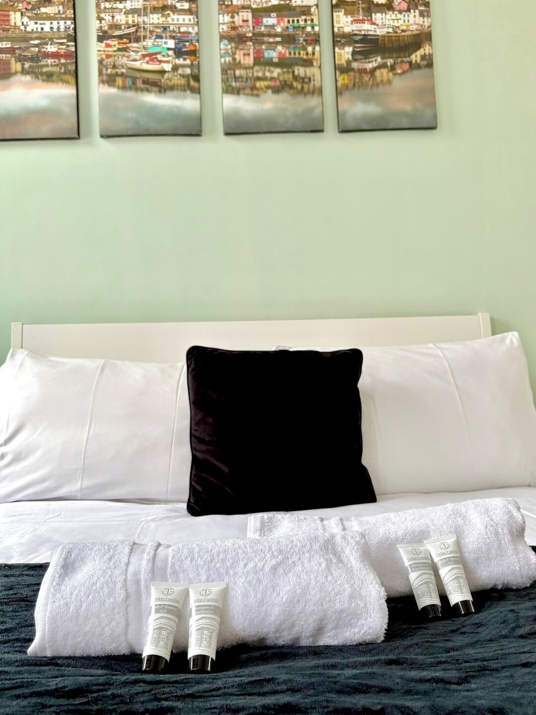 A hotel room with a bed, white and black pillows, a view of a cityscape through the window, and toiletries on the bed.