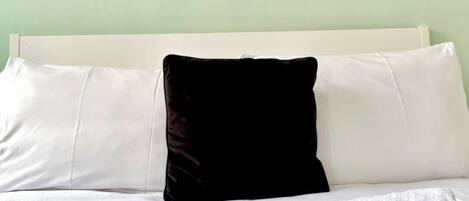 A hotel room with a bed, white and black pillows, a view of a cityscape through the window, and toiletries on the bed.