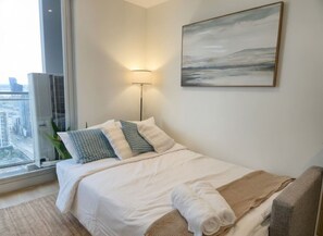 Quarto de hotel com cama, luminária, pintura e vista da cidade pela janela.