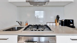 Cozinha moderna com fogão a gás, pia de aço inoxidável e armários brancos.