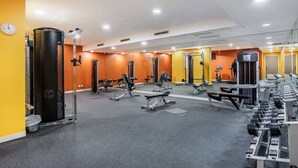 Uma academia com diversos equipamentos de exercício, um relógio na parede e um espelho refletindo o espaço.