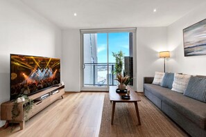 A modern living room with a flat-screen TV, a sofa, a coffee table, and a large window with a view of the city. - Stunning L34 views | Pool, Sauna, Gym | Sth Cross (Melbourne)