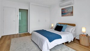 Quarto com cama, luminárias de cabeceira, um quadro e um ar-condicionado.