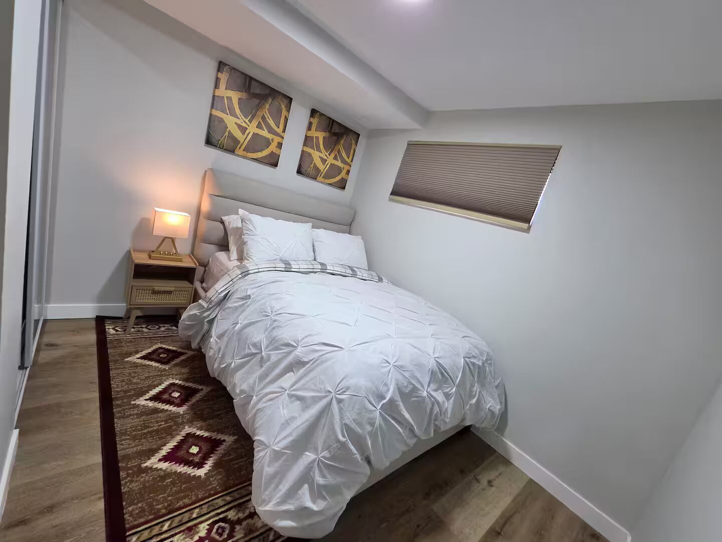 A bedroom with a bed, nightstand, lamp, and a patterned rug.