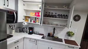 Una cucina moderna con mobili bianchi, un lavello in acciaio inossidabile, una macchina da caffè e diversi utensili da cucina.