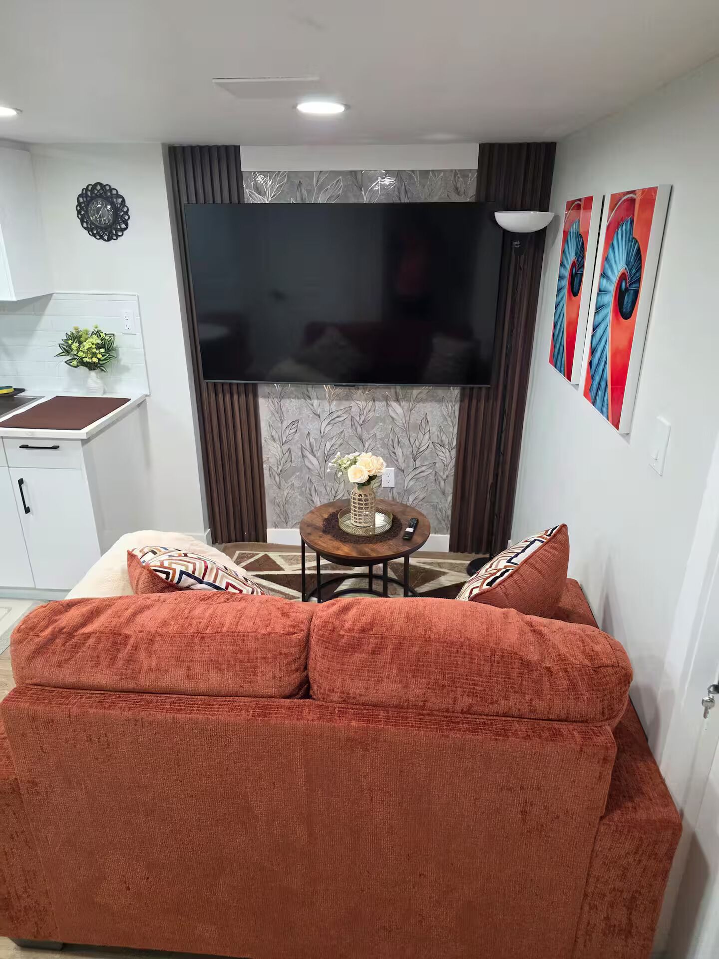 A living room with a sofa, a small table with a vase, a flat-screen TV, and a decorative wall piece.