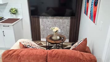 A living room with a sofa, a small table with a vase, a flat-screen TV, and a decorative wall piece.