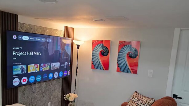 Un soggiorno con una televisione a schermo piatto che mostra una serie di fantascienza, un divano rosso, un tavolino rotondo con un vaso e due opere d'arte astratte appese alle pareti.