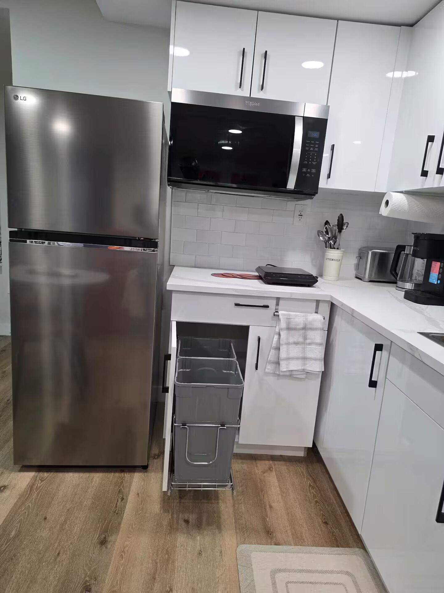 A modern kitchen with stainless steel appliances, white cabinetry, and a microwave.