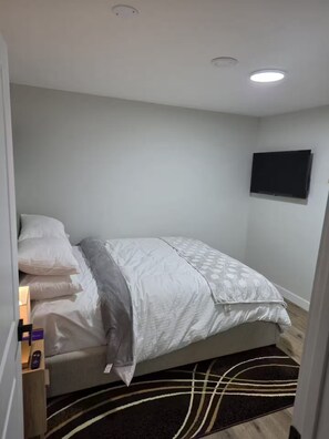 A bedroom with a bed, bedside table, and a mounted TV. - Modern Private 2-Bedroom Suite | Self Check-In | Free Parking (Winnipeg)