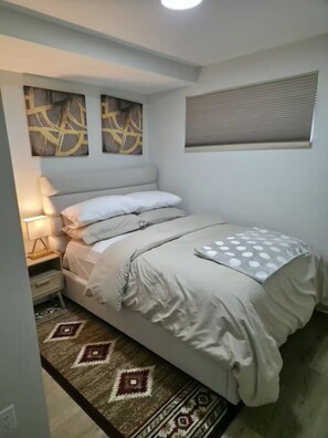A bedroom with a bed, a nightstand, a lamp, and a patterned rug. - Modern Private 2-Bedroom Suite | Self Check-In | Free Parking (Winnipeg)