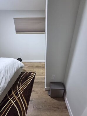 A bedroom with a bed, a rug, a radiator, and a trash bin.