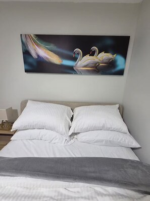 A bedroom with a bed, pillows, and a wall-mounted painting of swans.