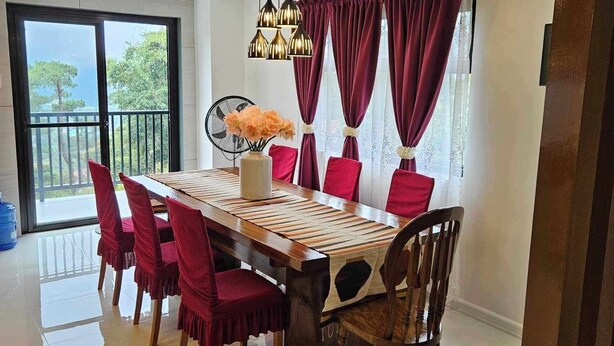 Zona pranzo con un tavolo grande, sedie rosse, un vaso con fiori e una ventola a soffitto.